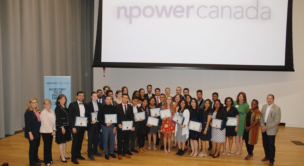 NPower Canada graduates holding their certificates with NPower coordinators in an auditorium after their graduation ceremony