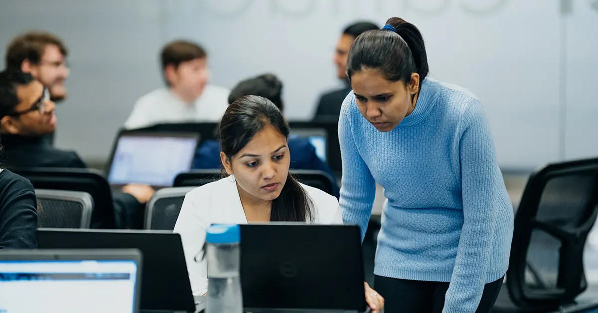 Image of two people looking at a laptop screen in a classroom